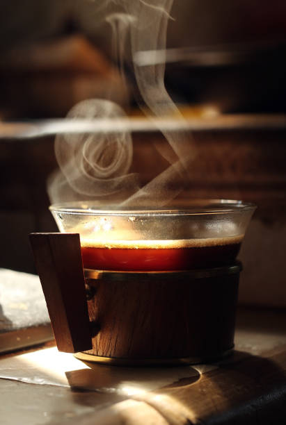 Small glass cup of hot black coffee with smoke on table.