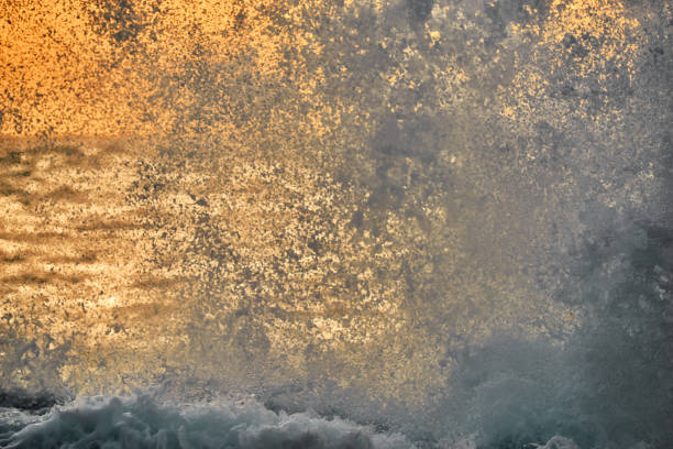 Splashing wave on sea in evening yellow light, cloudy sky, defocused