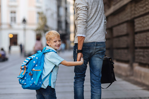 Young blond boy walking to school while holding dad's hand