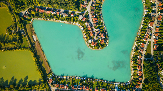 Drone point of view of a luxurious residential area with houses around a turquoise coloured lake. The lakes has the shape of a heart.