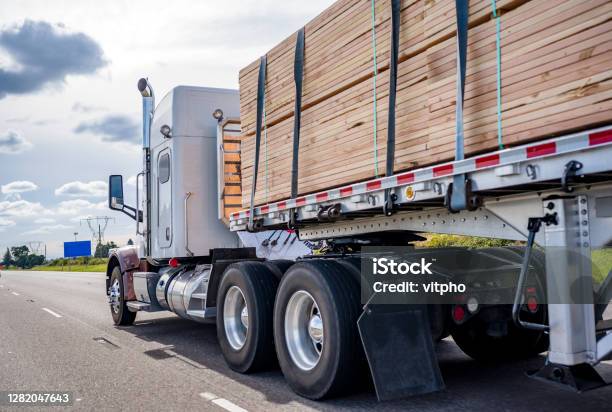 Classic Big Rig Semi Truck Tractor Transporting Lumber On The Flat Bed Semi Trailer Moving On The Wide Highway Road Stock Photo - Download Image Now