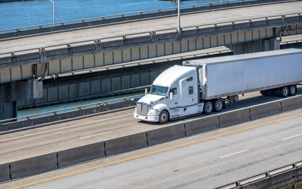 istock White bonnet big rig semi truck tractor transporting cargo in refrigerated semi trailer running on the multilevel overpass road intersection along the river 1282047648