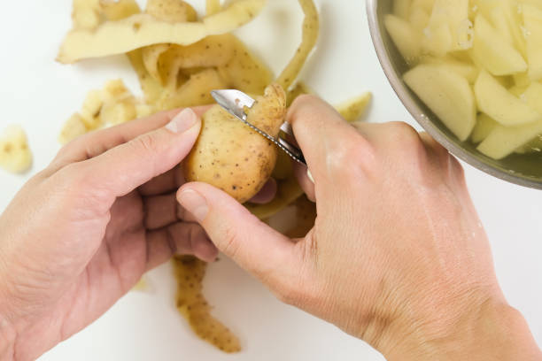 ręce gospodyni domowej obierania surowego ziemniaka specjalnym nożem narzędziowym z bliska, widok z góry - root vegetable raw potato human skin root zdjęcia i obrazy z banku zdjęć