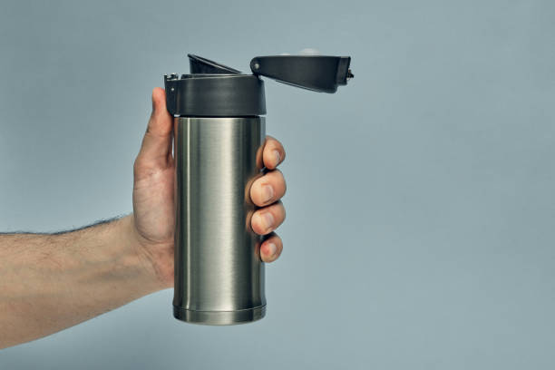 istock Metal mug thermos in hand on a colored background. Hot drinks on the go. Thermo mug. 1282053963