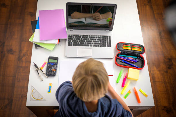 istock Young boy sitting at table with laptop computer and school supplies. 1282054716