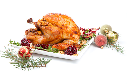 Pomegranate glazed roasted turkey on a tray garnished with fresh pomegranates, herbs, and walnuts over white background. Christmas ornaments and fir twigs.