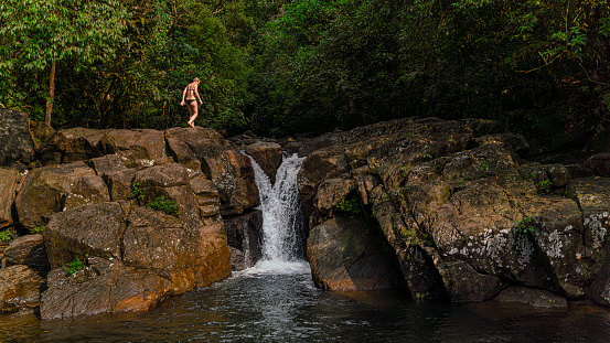 Tropical vacations in Sri Lanka. Mature Caucasian White woman walking on rocks around a small waterfall.