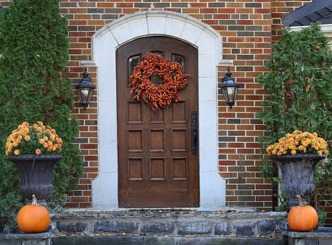 wooden front door of brick house with fall decorative wreath and pumpkins