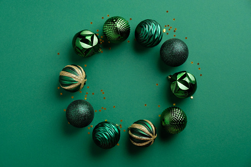 Christmas wreath made of balls decoration on green background. Flat lay style composition, top view.
