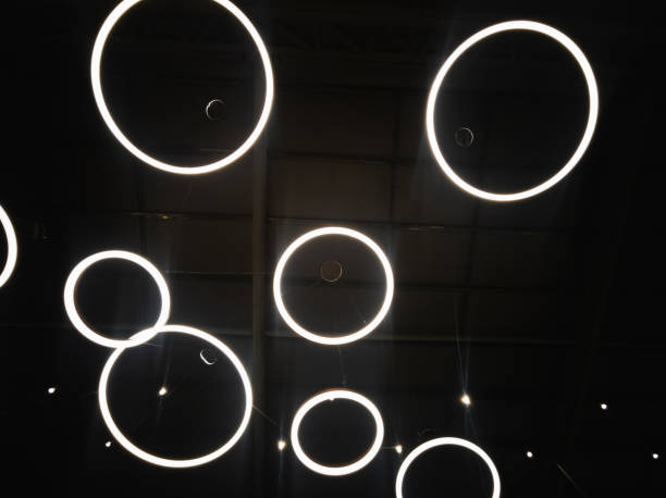 White circular ring shaped lamps hang under a concrete ceiling with external wiring