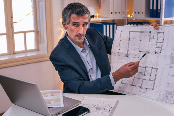 istock Active seniors at work career. Businessman working in his office. Handsome architect showing his project to the client through the internet during COVID-19 pandemic. Flatten the curve. 1282083423