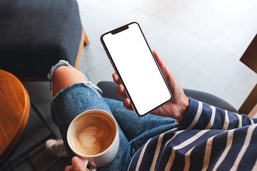 Mockup image of a woman holding mobile phone with blank screen while drinking coffee