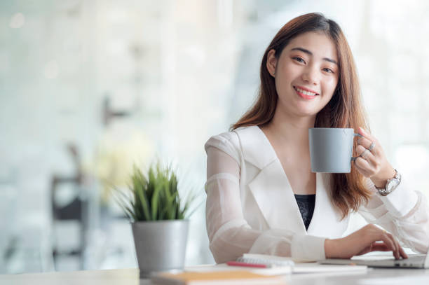 istock Portrait of female office worker drinking coffee while working with laptop on worktable in office room 1282091828