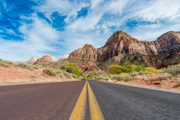 Front view photography from a car driving on an asphalt road with yellow lines through Zion National Park in Utah, USA.