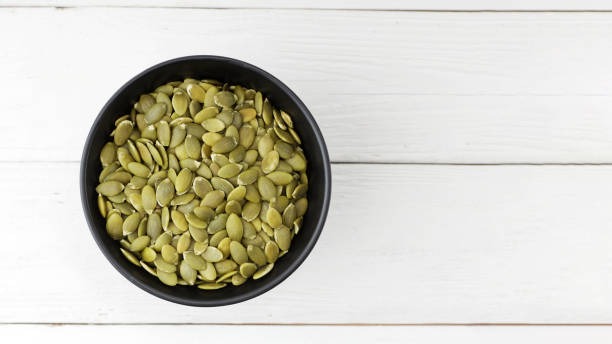 istock Pumpkin seeds in black bowl on white wooden table. Top view. Copyspace. 1282102239