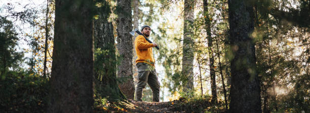 istock Man lumberjack with axe in forest. Strong bearded lumberman wearing work clothes holds axe on his shoulder. Wide image 1282104949