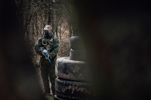 Paintball player aiming and shooting in autumn forest. Photo from the real game.