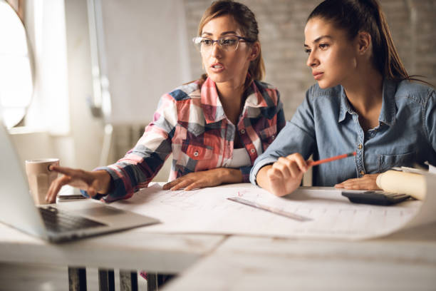 istock Young creative businesswomen  working on blueprints in the office 1282108373