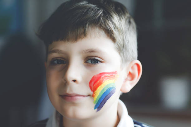 顔にカラフルな色で虹を描いた愛らしい学校の子供の少年の肖像画。パンデミックコロナウイルス検疫中の孤独な子供。子供たちは世界中で虹を作り、描く - epidemic paint virus illness ストックフォトと画像