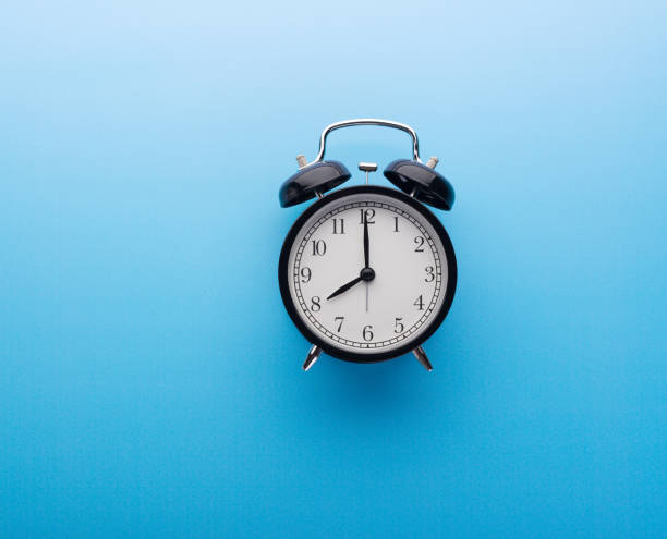 istock Black retro alarm clock top view, isolated on blue background. Time and morning concept 1282112615
