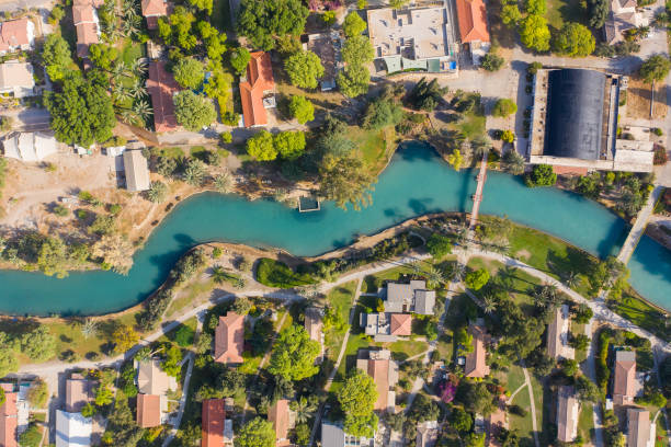 Aerial pass over Kibbutz Nir David with Asi river channel turquoise water dividing east and west side riverside houses and palm trees, Israel. Aerial pass over Kibbutz Nir David with Asi river channel turquoise water dividing east and west side riverside houses and palm trees, Israel. nir stock pictures, royalty-free photos & images