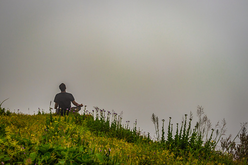 man meditating on rock isolated at the serene nature with white cloud background image is showing the breathtaking beauty of nature at south india.