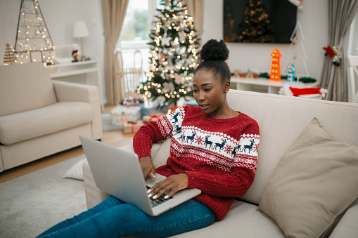 Beautiful African American female student sitting at home, working using her laptop during winter holidays