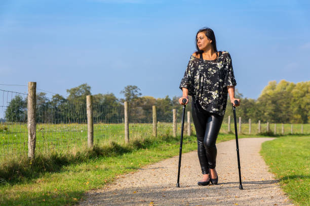 Disabled young woman walks on crutches on rural footpath Disabled young woman walking on crutches outside on hiking trail in european park. The moluccan person is enjoying the sunny weather dring autumn season in the Netherlands. disabled person hiking outdoors stock pictures, royalty-free photos & images