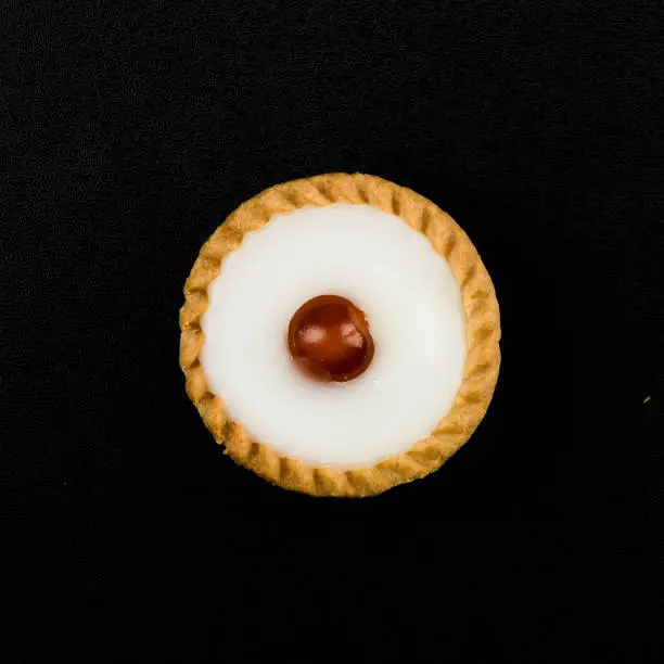 Top View Close Up Of A Freshly Baked Bakewell Tart With A Single Glazed Cherry, Isolated On A Black Background With No People