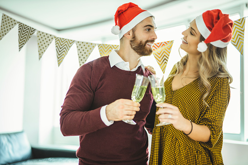 Couple celebrating New Years, holding glasses of champagne and toasting to each other at home