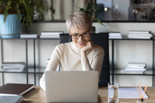 istock Smiling young woman busy working on laptop in office 1282120068