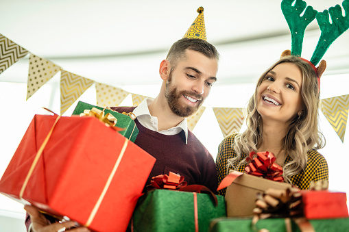 Portrait of young couple holding Christmas present and celebrating New Year at home