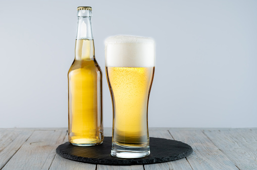 A glass of light beer on a tray. Bottle and glass of light beer. Beer on the table.