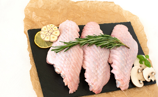 raw parts of turkey wing, three pieces of chicken, on black stone cutting board with limes and parsley on a white background, isolate