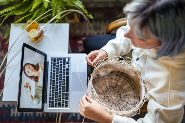 Young Blue haired woman knitting a wicker pot at home using laptop for watching online tutorial