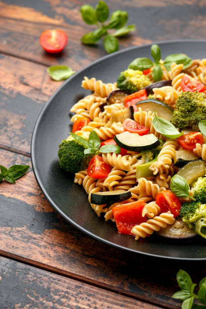 istock Fusilli pasta with vegetable, broccoli, zucchini, red pepper, eggplant, tomato and basil on black plate 1282125547