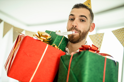 Portrait of young beautiful man celebrating New Year and holding Christmas presents at home