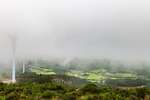 Aerial view of the Ria de Muros y Noya estuary from the Muralla mountain on a foggy Summer afternoon, with some wind turbines among the clouds.