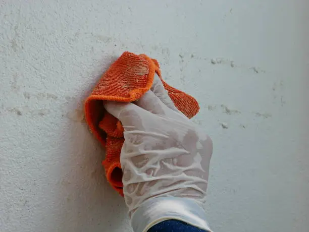 Photo of A piece of cloth, soaked with thinner, in a hand of a painter being used to remove sticky rough glue and tape remain on the old concrete wall, as a preparation before starting the paint the house