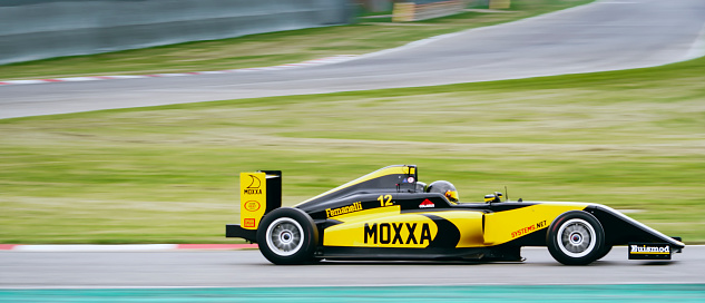 Blurred motion of racing driver driving yellow open-wheel single-seater racing car car on motor racing track.