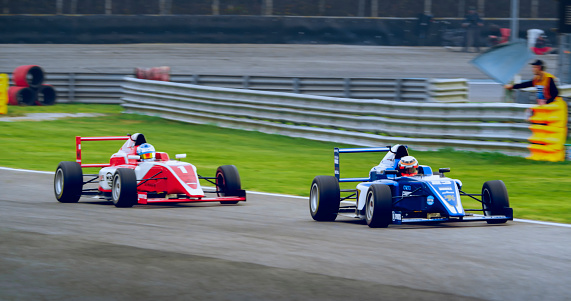 Racing drivers driving red and blue open-wheel single-seater racing car cars on racing track.