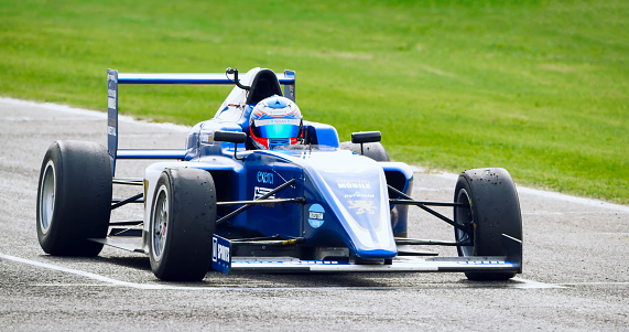 Racing driver driving blue open-wheel single-seater racing car car on racing track.