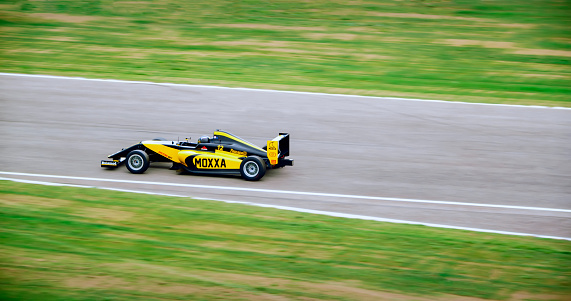 Blurred motion of racing driver driving yellow open-wheel single-seater racing car car on racing track.