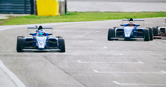 Racing drivers driving blue open-wheel single-seater racing car cars on racing track.