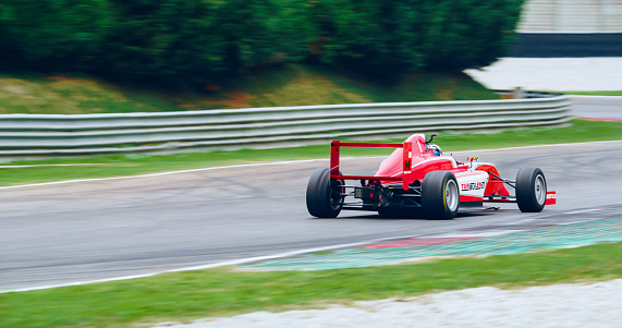 Racing driver driving red open-wheel single-seater racing car car on racing track.