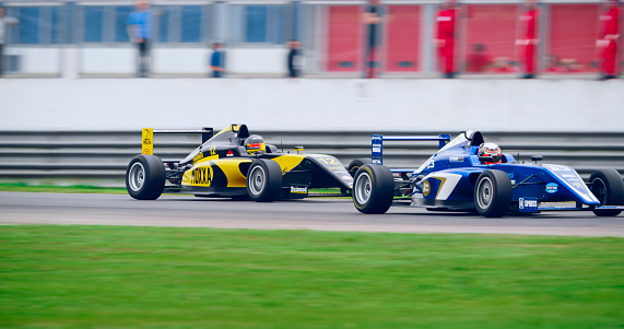 Racing drivers driving blue and yellow open-wheel single-seater racing car cars on racing track.