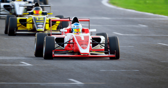 Racing drivers driving red and yellow open-wheel single-seater racing car cars on racing track.