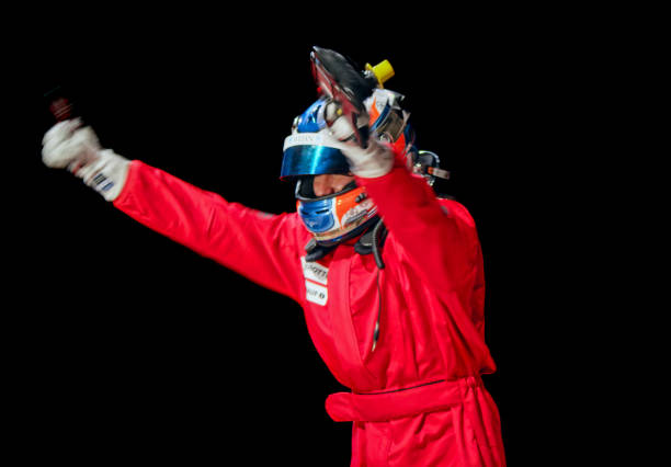 Cheerful racing driver raising his arms while celebrating his victory against black background.