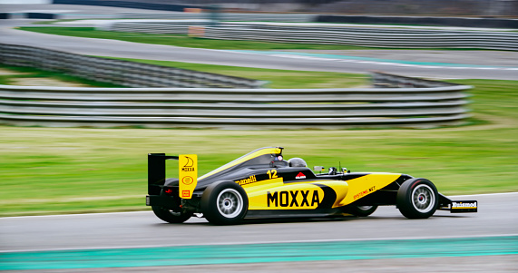 Blurred motion of racing driver driving yellow open-wheel single-seater racing car car on racing track.