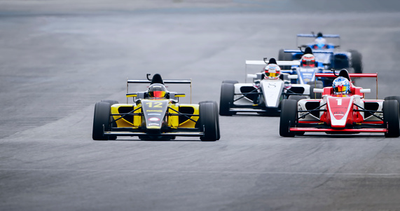 Racing drivers driving open-wheel single-seater racing car cars on racing track.